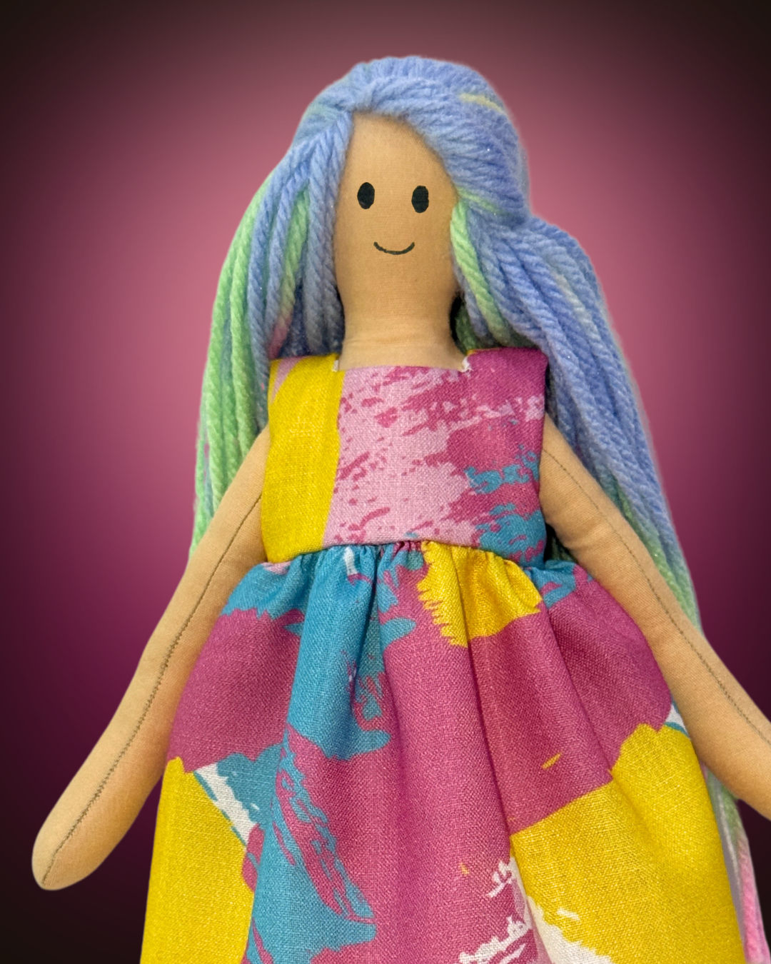Sustainable soft doll with pastel rainbow hair, wearing a playful multicolored splash-print dress, plastic-free and safe for kids